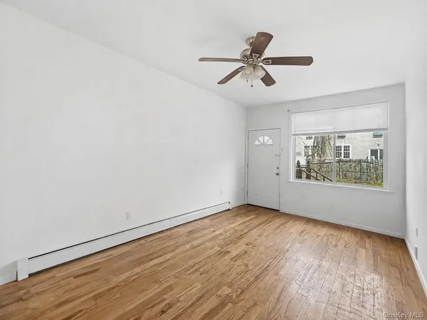 an empty room with wooden floor fan and windows