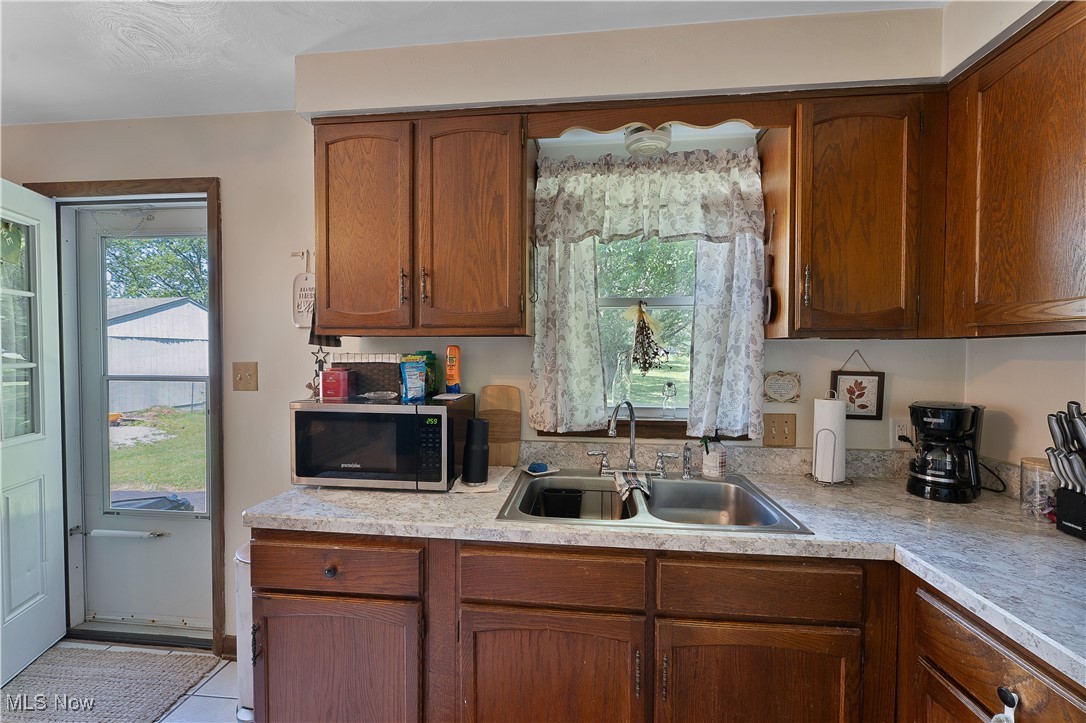 9925 Struthers Road New Middletown, OH 44442 - Photo 5 of 12 Kitchen featuring light countertops, stainless steel microwave, light tile patterned flooring, and brown cabinets
