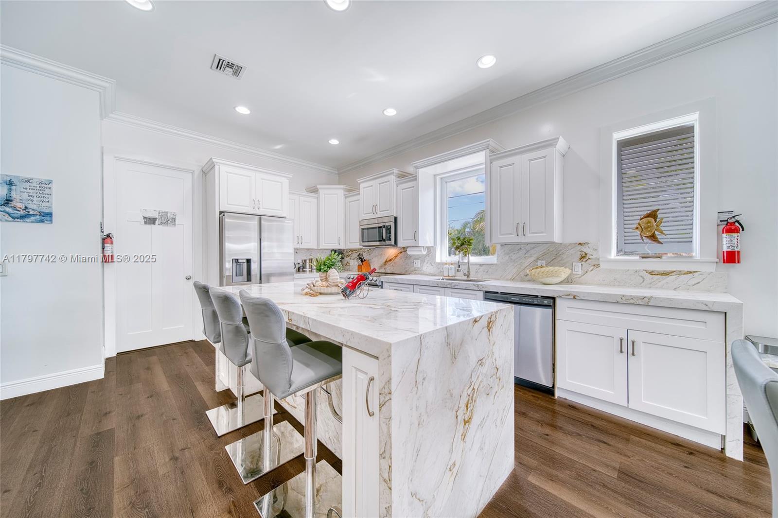 207 Southwest 11th Street Dania Beach, FL 33004 - Photo 15 of 37 a kitchen with stainless steel appliances kitchen island granite countertop a table chairs sink and white cabinets