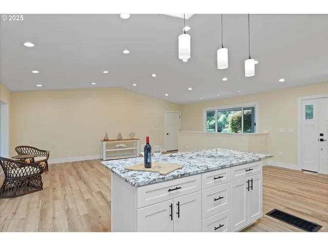 a room with stainless steel appliances kitchen island granite countertop a stove a sink a refrigerator and white cabinets with wooden floor