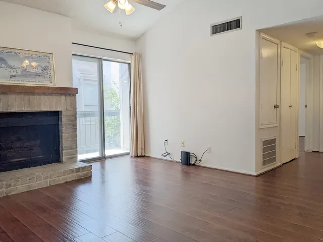 a view of an empty room with wooden floor fireplace and a window