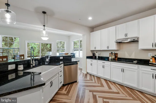 a large white kitchen with granite countertop a sink a counter top space stainless steel appliances and cabinets