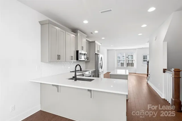 a kitchen with stainless steel appliances a sink a stove and white cabinets with wooden floor