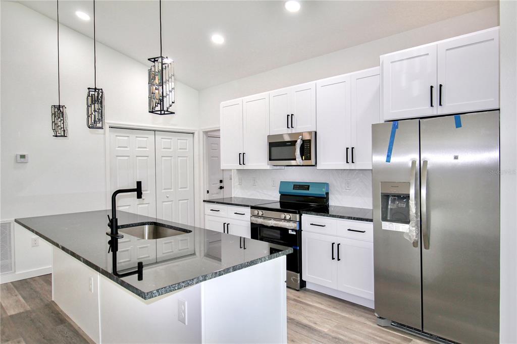 454 Bonnie Road Northwest Lake Placid, FL 33852 - Photo 3 of 30 a kitchen with stainless steel appliances granite countertop a sink a stove a refrigerator and island with wooden floor