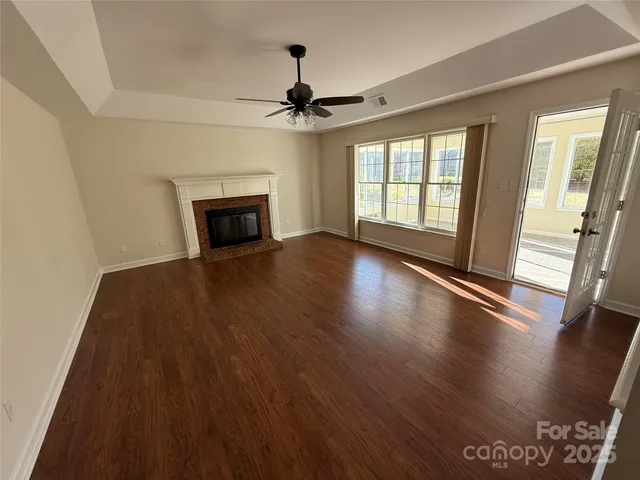 a view of a livingroom with wooden floor a fireplace a ceiling fan and window