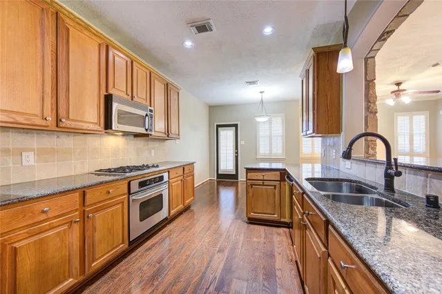 a kitchen with stainless steel appliances granite countertop wooden cabinets a sink and dishwasher a stove with wooden floor