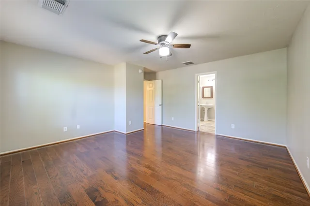 a view of an empty room with wooden floor and a ceiling fan