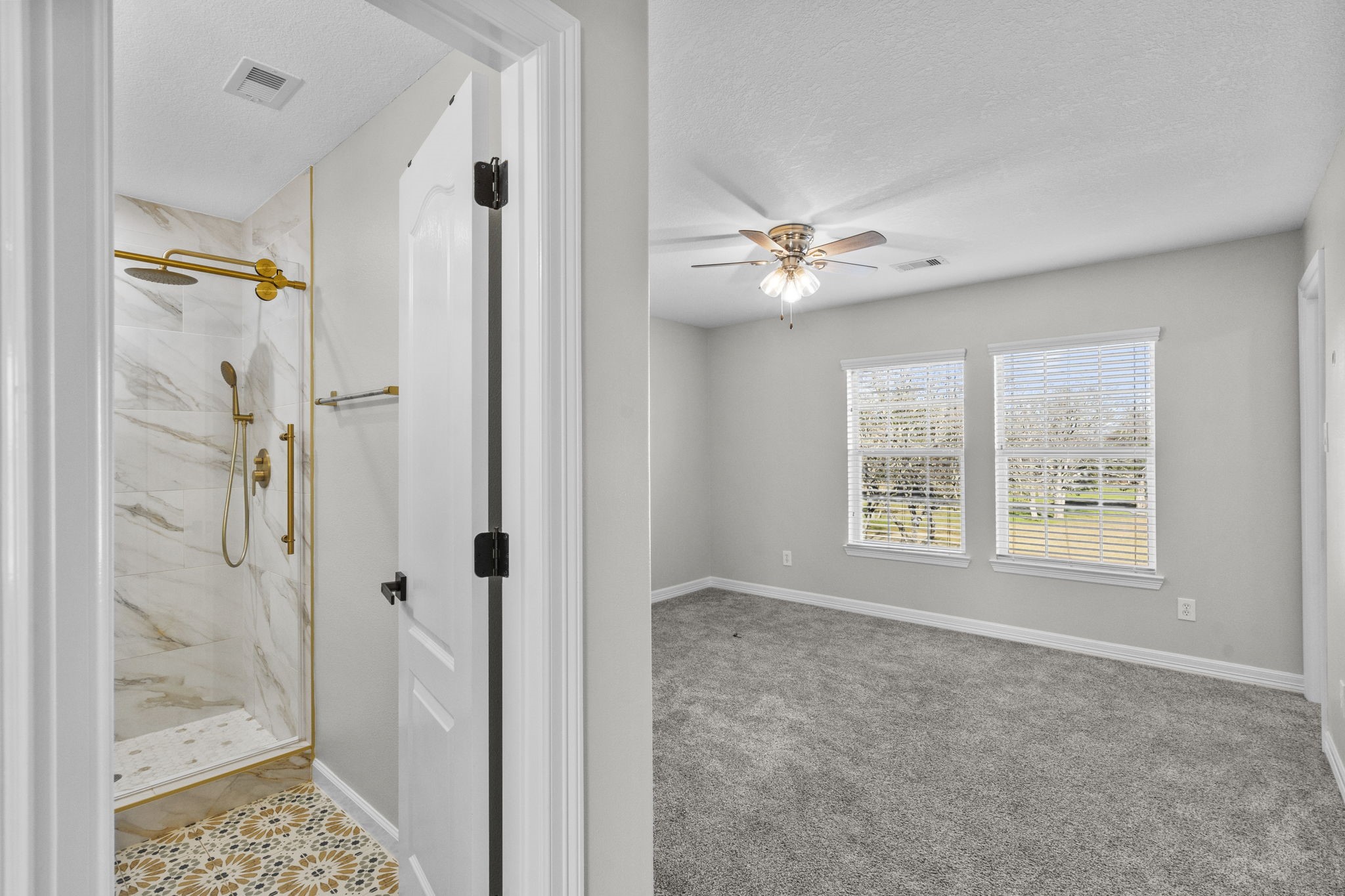 2730 Lawrence Road Kemah, TX 77565 - Photo 33 of 46 This photo shows a bright bedroom with carpeted flooring and a ceiling fan, adjacent to a modern bathroom featuring a marble-tiled shower with gold fixtures.