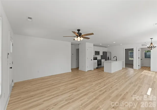 a view of empty room with wooden floor and kitchen view