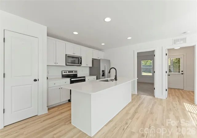 a large white kitchen with stainless steel appliances granite countertop a stove a sink and a refrigerator
