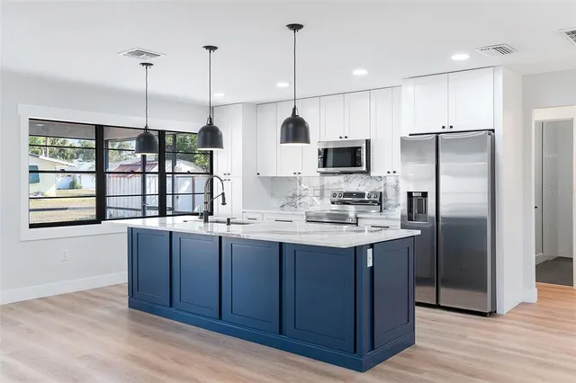 a kitchen with stainless steel appliances kitchen island granite countertop a refrigerator a sink and a wooden floor
