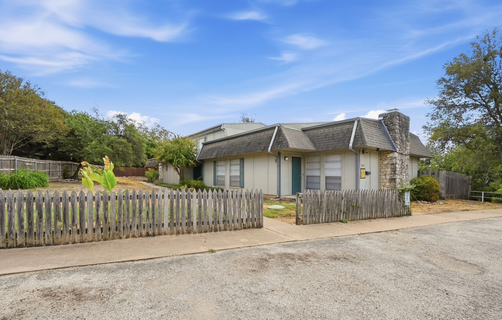 Rustic wooden fencing surrounds this multi-level home featuring a prominent stone chimney and mansard roofline.