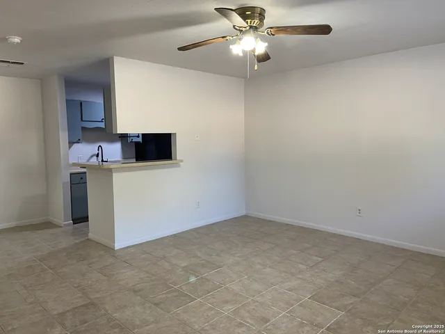 an empty room with a kitchen and a ceiling fan
