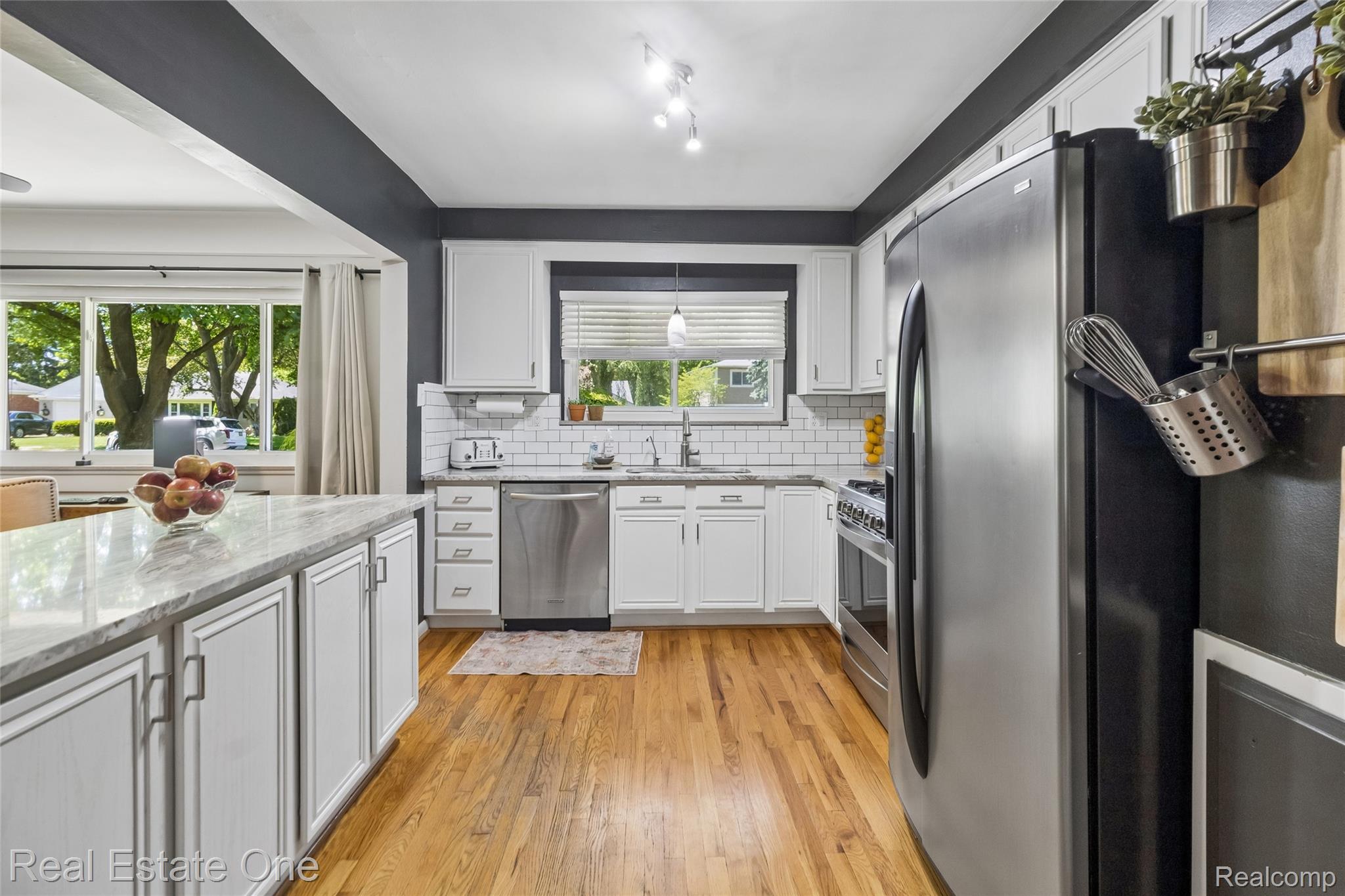 2189 Devonshire Road Bloomfield Hills, MI 48302 - Photo 11 of 50 Kitchen featuring white cabinetry, wood-finish flooring, stainless steel appliances, a white subway tile backsplash, and a large island with a stone countertop