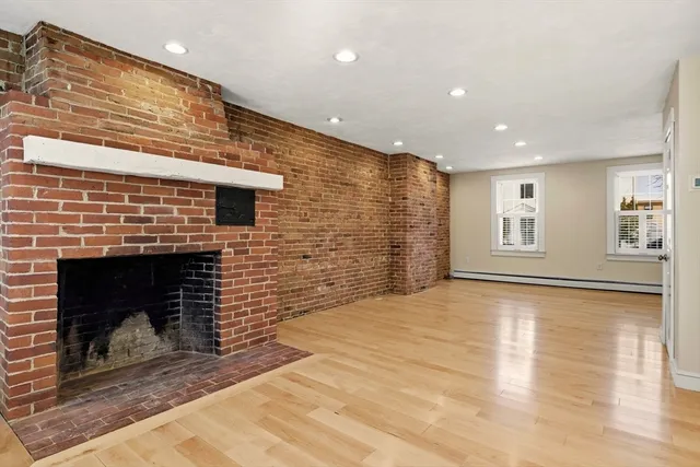 a view of an empty room with wooden floor fireplace and a window