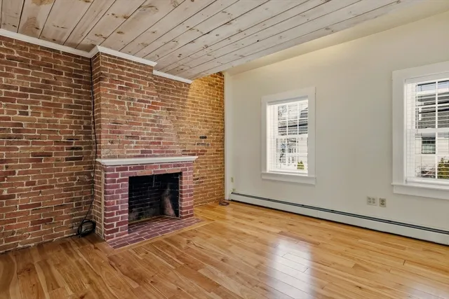 a view of an empty room with wooden floor fireplace and a window
