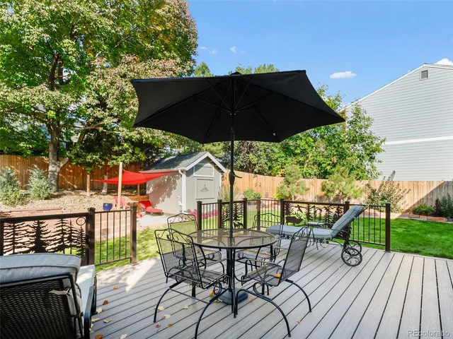 a view of a roof deck with table and chairs under an umbrella with wooden floor and fence