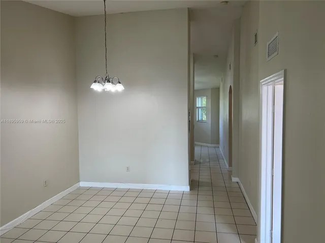 an empty room with chandelier fan and kitchen view