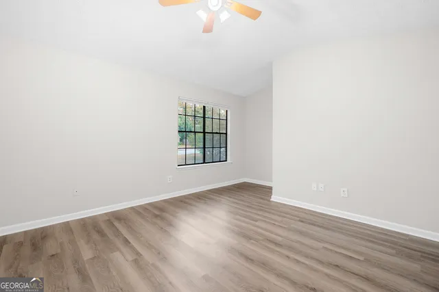 an empty room with wooden floor fan and windows