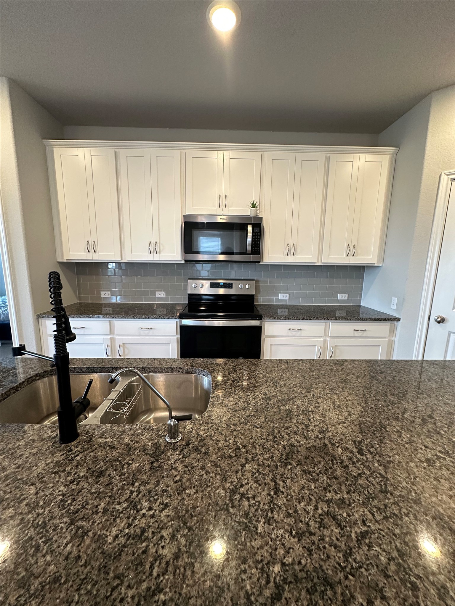13000 Titanium Street Austin, TX 78754 - Photo 3 of 15 Kitchen featuring granite countertops, white cabinetry, a subway tile backsplash, stainless steel microwave, and a black electric range