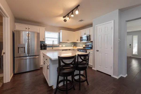 a kitchen with stainless steel appliances granite countertop a dining table chairs refrigerator and microwave