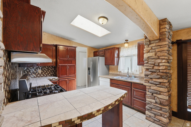 2875 North Hill Field Road, Unit 111 Layton, UT 84041 - Photo 9 of 30 Kitchen featuring a peninsula, tile counters, light tile patterned floors, lofted ceiling, and a skylight