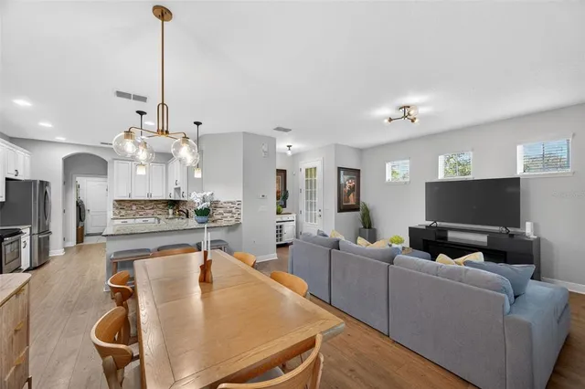 a kitchen with stainless steel appliances granite countertop a stove a refrigerator a sink a dining table and chairs with wooden floor