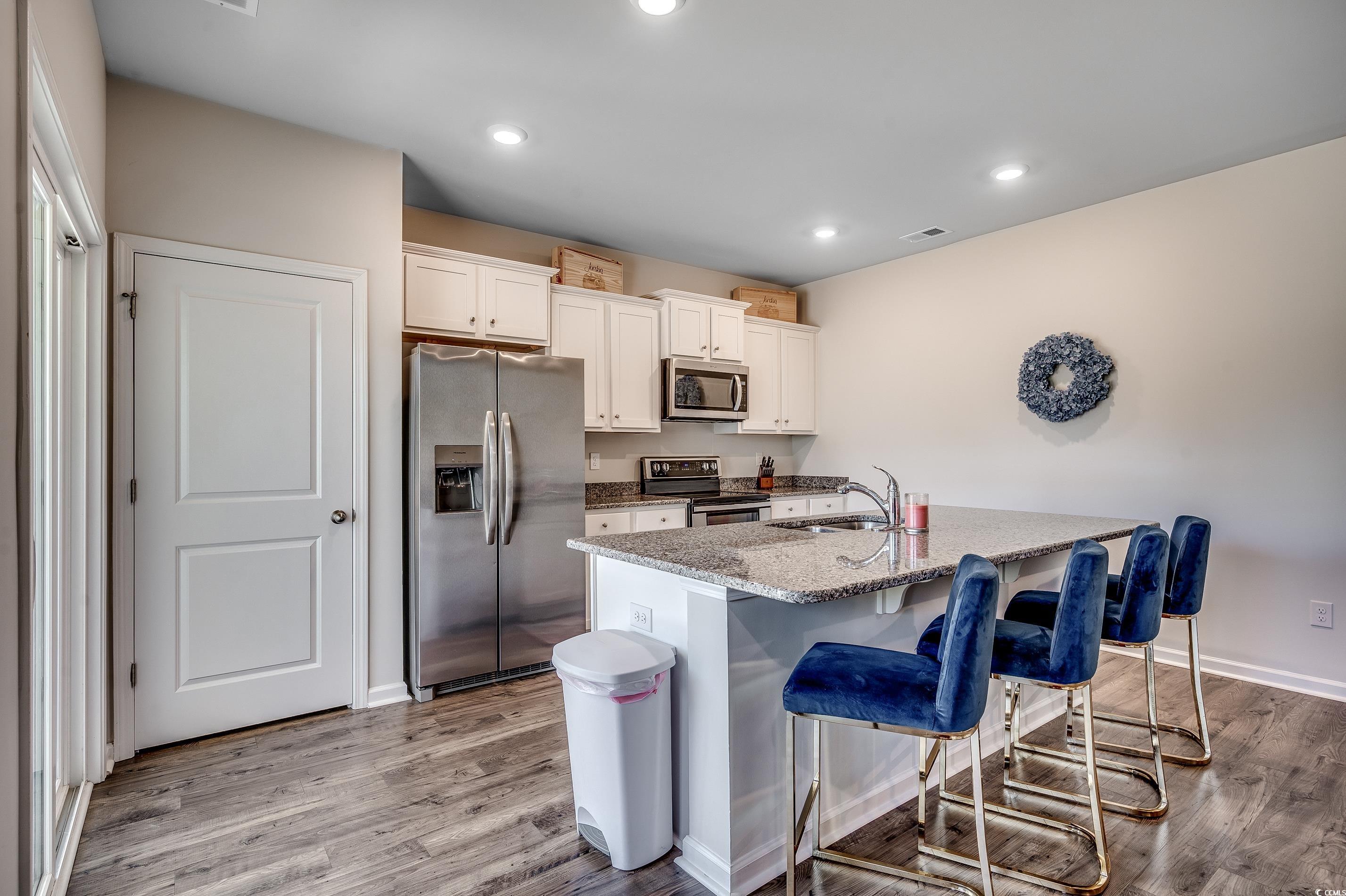 2924 Skylar Drive Myrtle Beach, SC 29577 - Photo 4 of 30 Kitchen with stainless steel appliances, a breakfast bar area, a center island with sink, light wood-type flooring, and light stone countertops