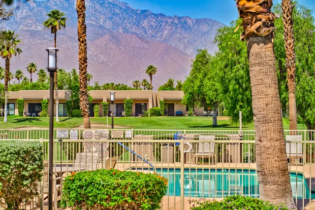 a view of a white house with a big yard and potted plants and large trees