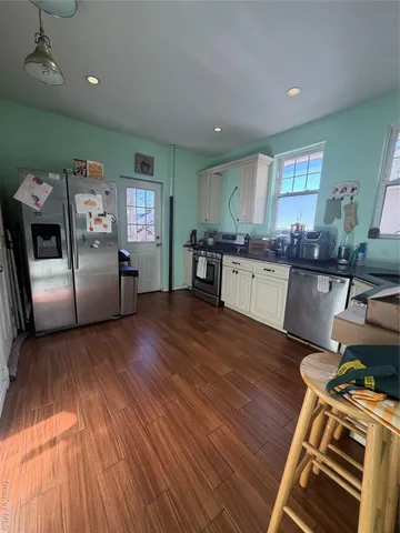 a kitchen with stainless steel appliances granite countertop a refrigerator a sink dishwasher a stove and a dining table with wooden floor