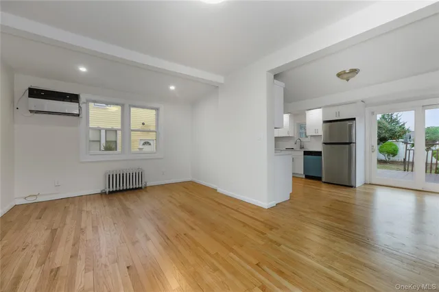 an empty room with wooden floor kitchen view and windows
