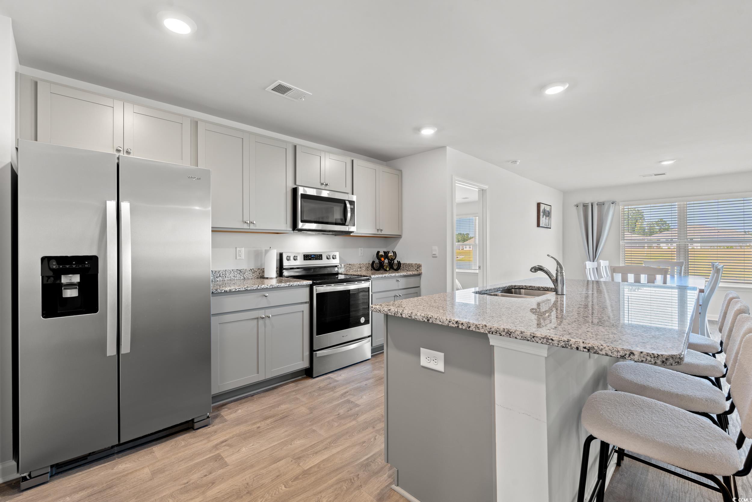 514 Strawberry Field Way Galivants Ferry, SC 29544 - Photo 2 of 37 Kitchen featuring appliances with stainless steel finishes, light stone counters, light wood-style floors, recessed lighting, and a kitchen bar
