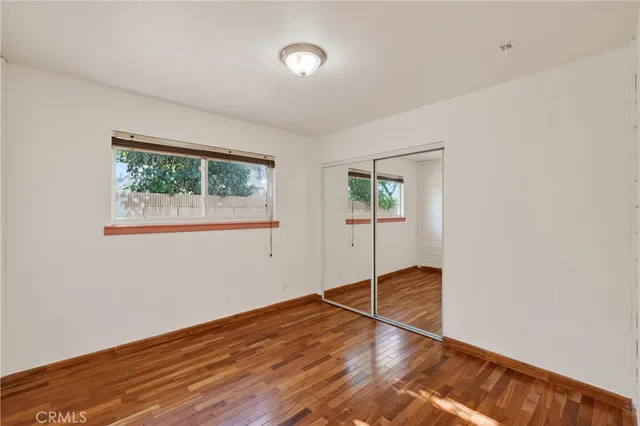 an empty room with wooden floor closet and windows