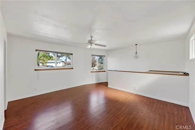 an empty room with wooden floor chandelier fan and windows
