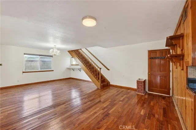 an empty room with wooden floor staircase and windows