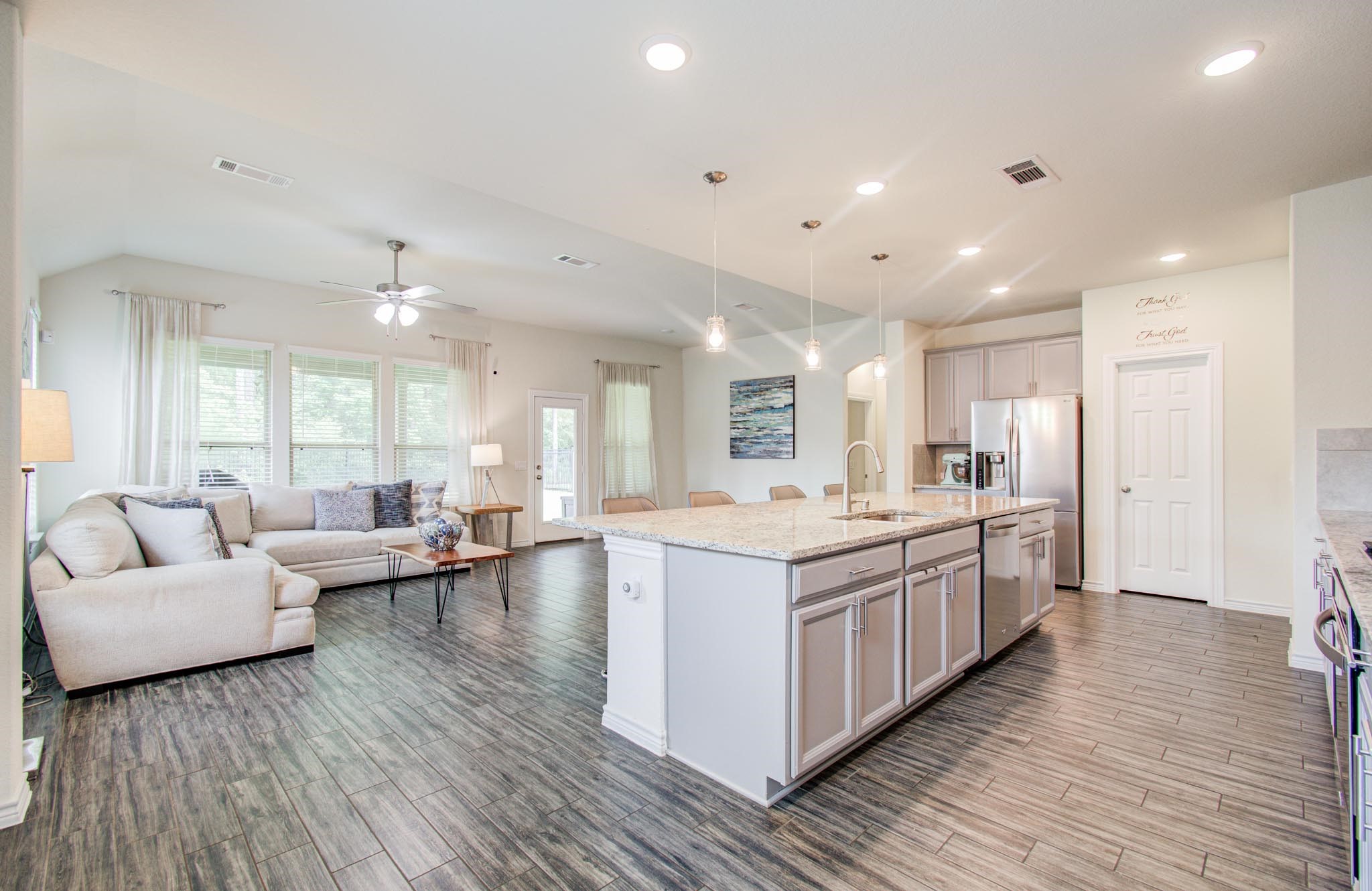 27817 Ellie Oak Lane Spring, TX 77386 - Photo 12 of 49 Open-concept living space with a modern kitchen featuring an island, stainless steel appliances, and pendant lighting. The adjacent living area includes a cozy sectional sofa, large windows for natural light, and wood-style flooring, creating a warm and inviting atmosphere.