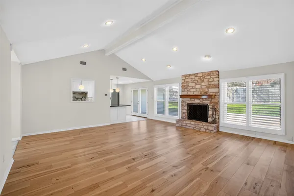 an empty room with wooden floor fireplace and windows