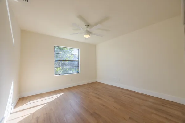 an empty room with wooden floor ceiling fan and windows