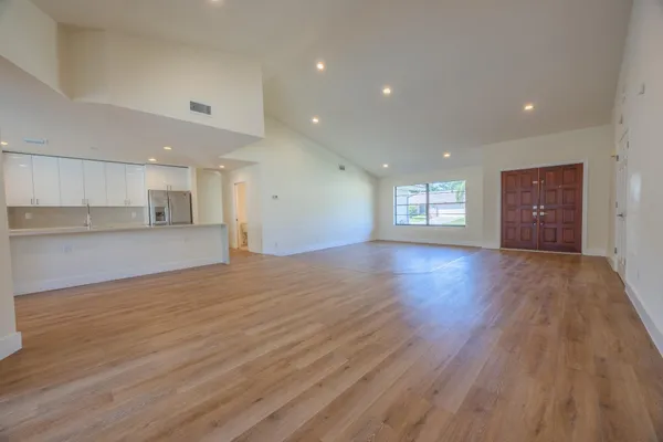 a view of an empty room and a kitchen with wooden floor