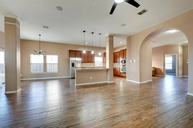a view of an empty room and kitchen with hardwood floor