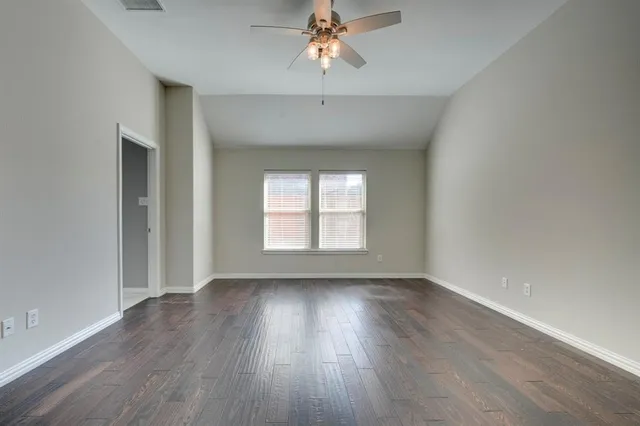 an empty room with wooden floor chandelier fan and windows