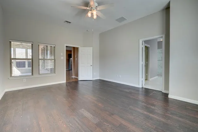 an empty room with wooden floor chandelier fan and windows