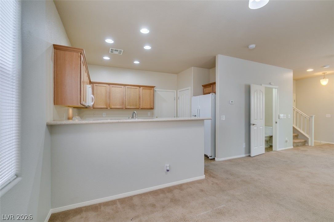 8937 Caledon Ridge Court Las Vegas, NV 89149 - Photo 19 of 43 A functional kitchen with light wood cabinetry and essential appliances opens to a carpeted living space.