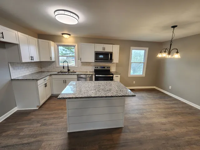 a kitchen with kitchen island granite countertop a stove a sink and white cabinets