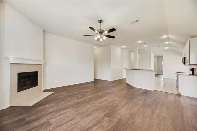 a view of an empty room with kitchen fireplace and a ceiling fan