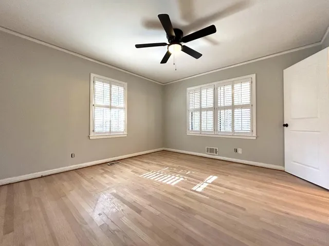 an empty room with wooden floor chandelier fan and windows