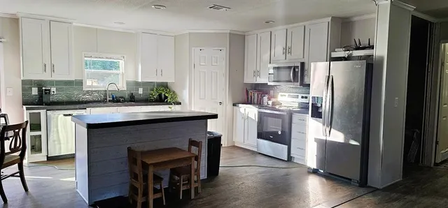 a kitchen with stainless steel appliances kitchen island granite countertop a refrigerator a stove a sink and white cabinets with wooden floor