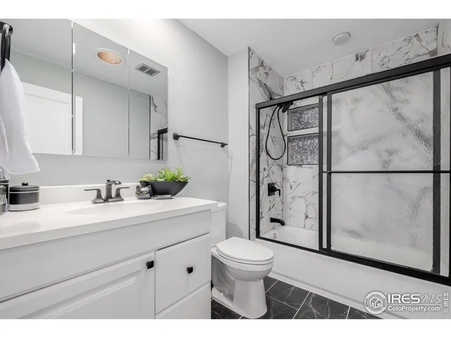 a bathroom with a granite countertop sink a toilet a mirror a vanity and shower