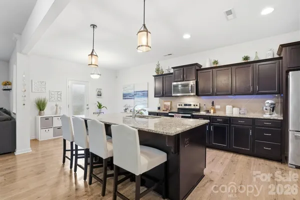 a kitchen with stainless steel appliances granite countertop a sink dishwasher a stove a refrigerator a dining table and chairs with wooden floor