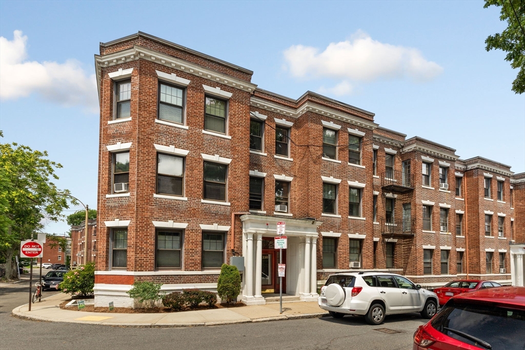 a front view of a building with lot of cars and trees